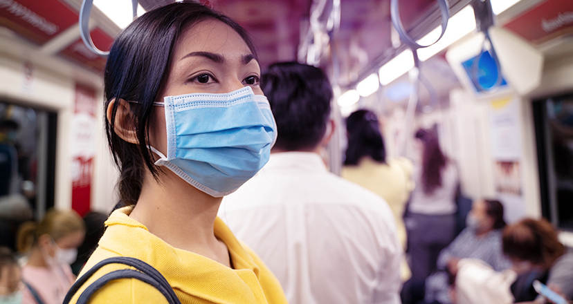 Frau mit medizinischer Maske im stark frequentierten öffentlichen Verkehrsmittel