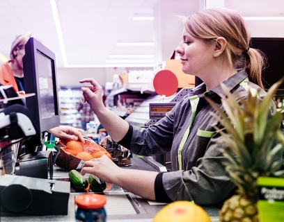 Eine Kassiererin im Supermarkt hat viel zu tun und kommt täglich mit vielen Menschen in Kontakt. #Gib8aufGrippeschutz.