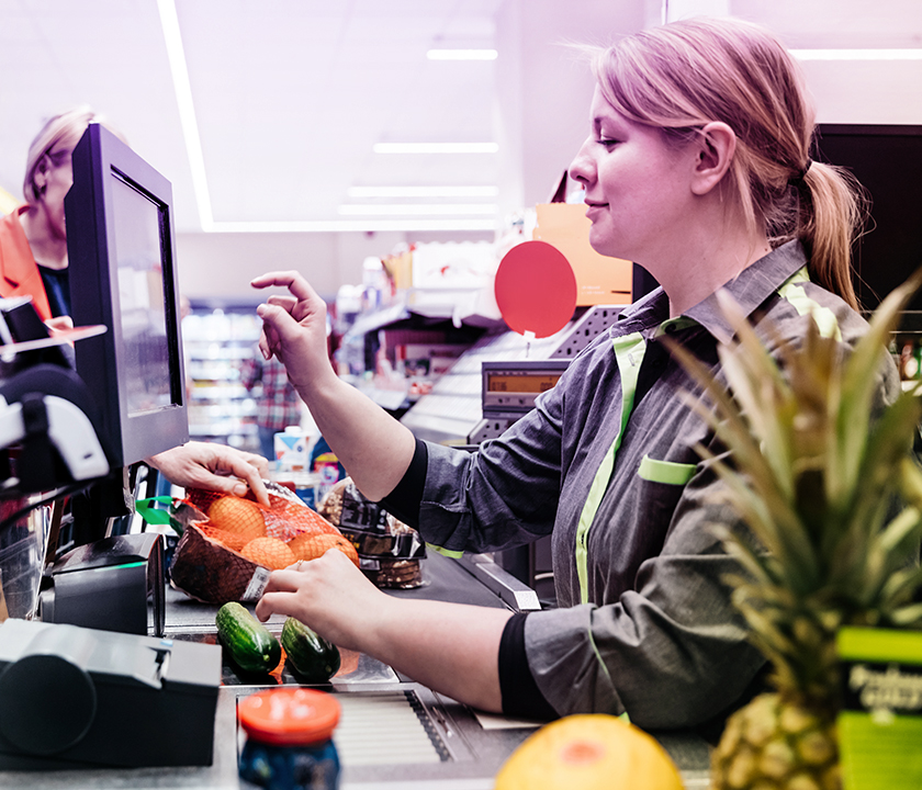 Eine Kassiererin im Supermarkt hat viel zu tun und kommt täglich mit vielen Menschen in Kontakt. #Gib8aufGrippeschutz.