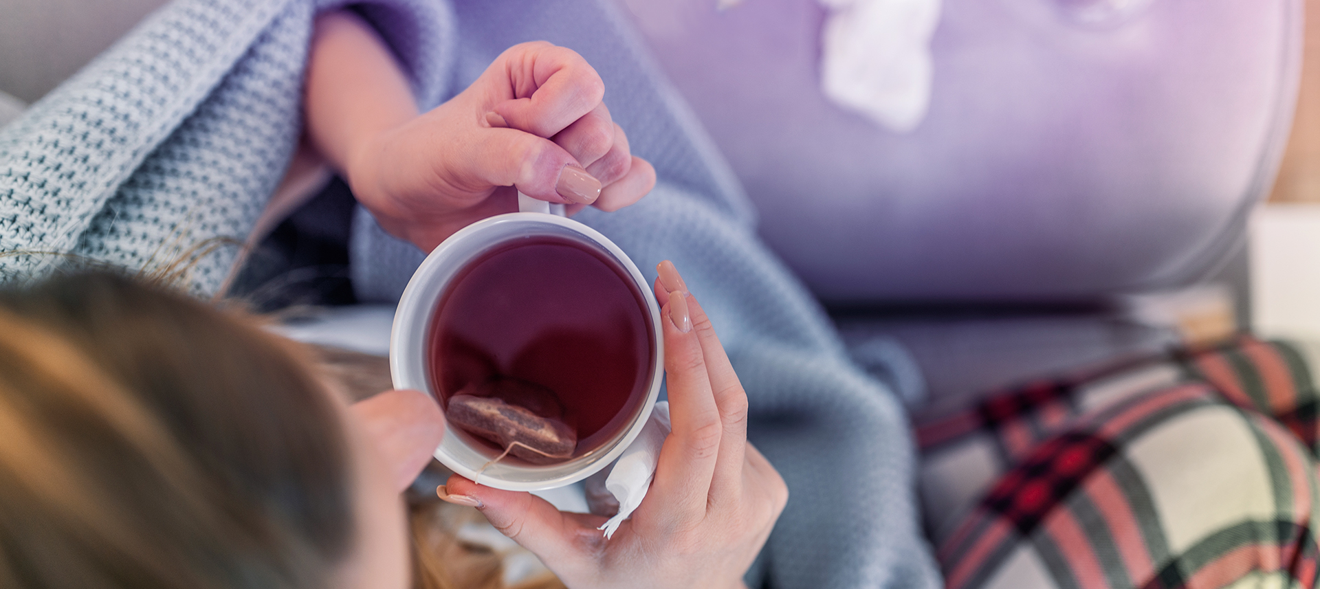 Erkrankte junge Frau sitzt mit Medikamenten auf dem Sofa und leidet an Grippesymptomen.