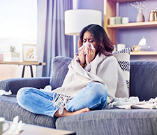 Frau sitzt auf dem Sofa und hat sich mit Grippe infiziert.