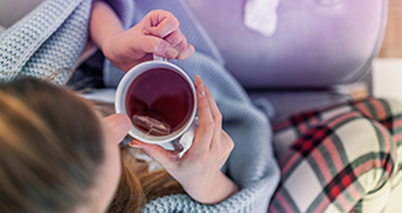Erkrankte junge Frau sitzt mit Medikamenten auf dem Sofa und leidet an Grippesymptomen.