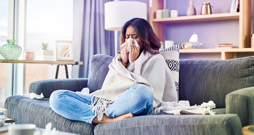 Frau sitzt auf dem Sofa und hat sich mit Grippe infiziert.