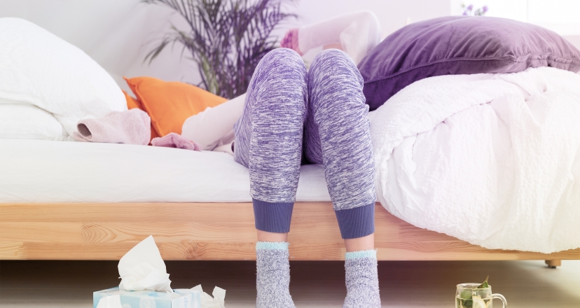 Frau hat sich mit Grippe infiziert und liegt erschöpft im Bett.